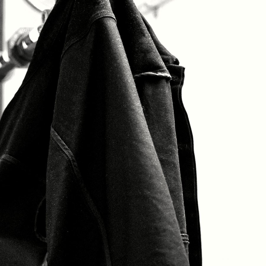 A dark jacket falling from a hanger against a white wall, photographed close.