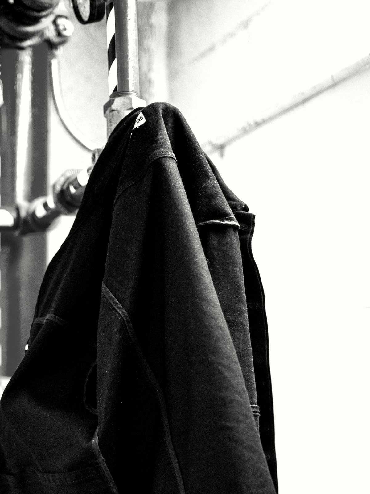A dark jacket hanging from a hook against a white wall.