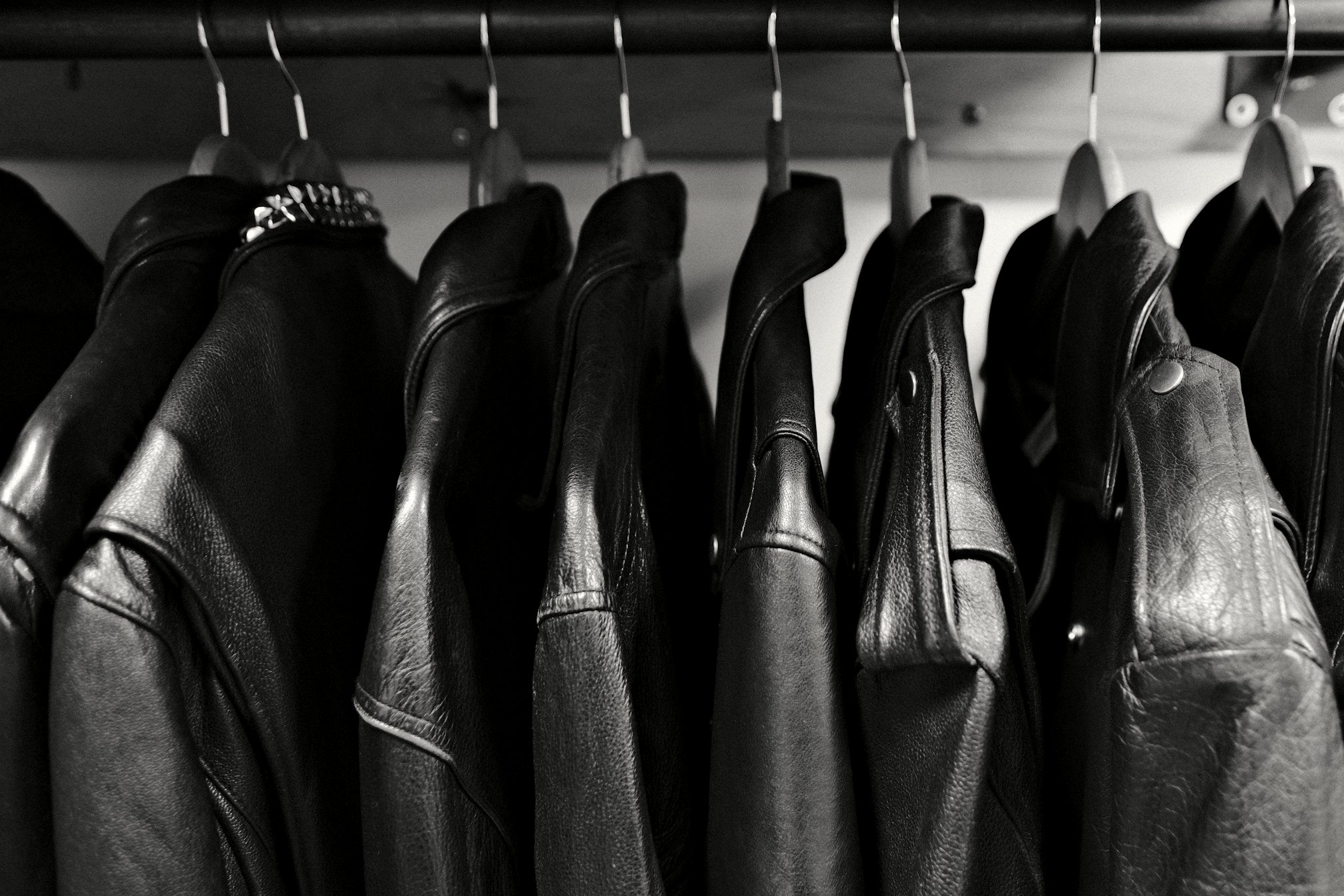 A dense row of black leather jackets hanging on a rail, photographed in black and white.