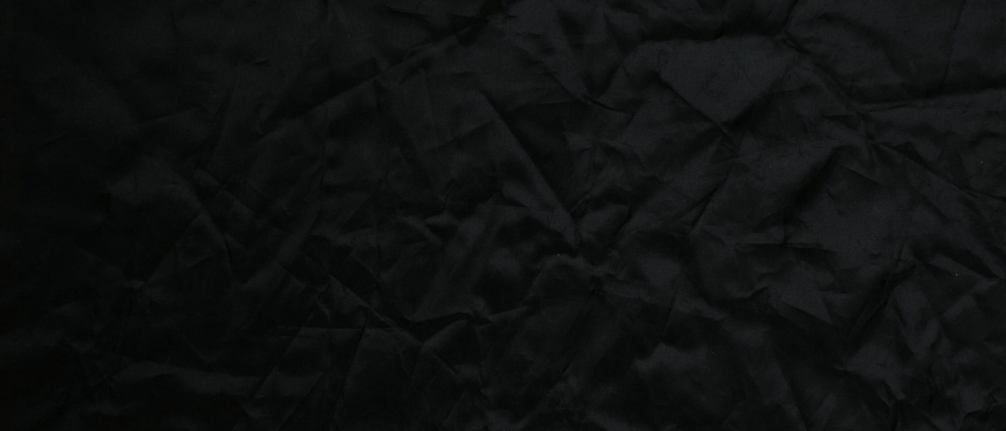 Black fabric filling the frame, creased and folded across itself.
